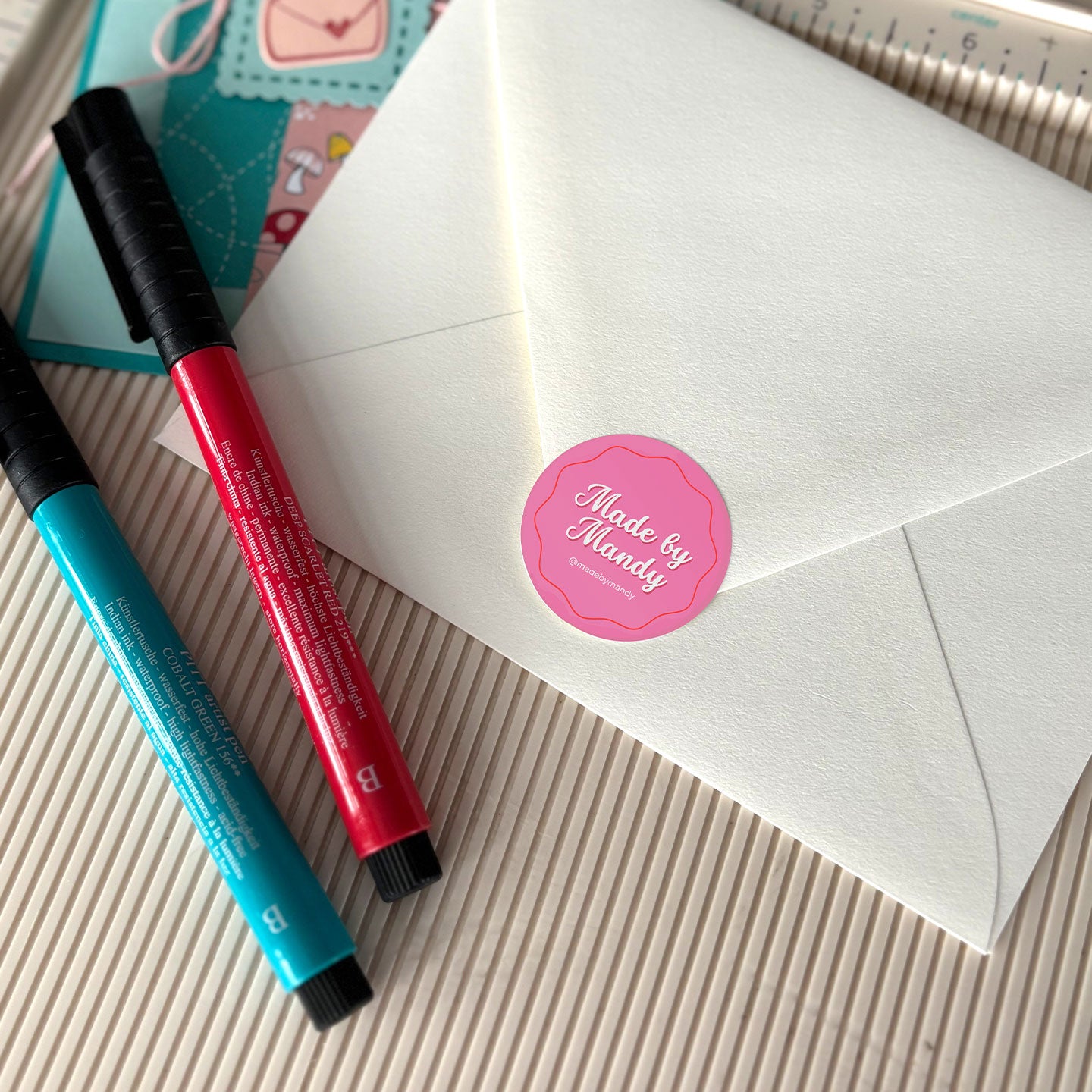 Circle label with custom artwork that reads, Made by Mandy, used on an envelope as a seal.